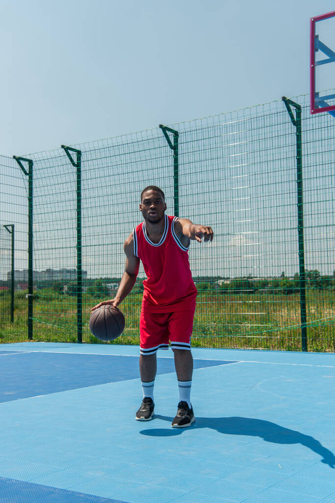 Sportivo afroamericano che punta con il dito mentre gioca a basket all'aperto  - Foto, immagini