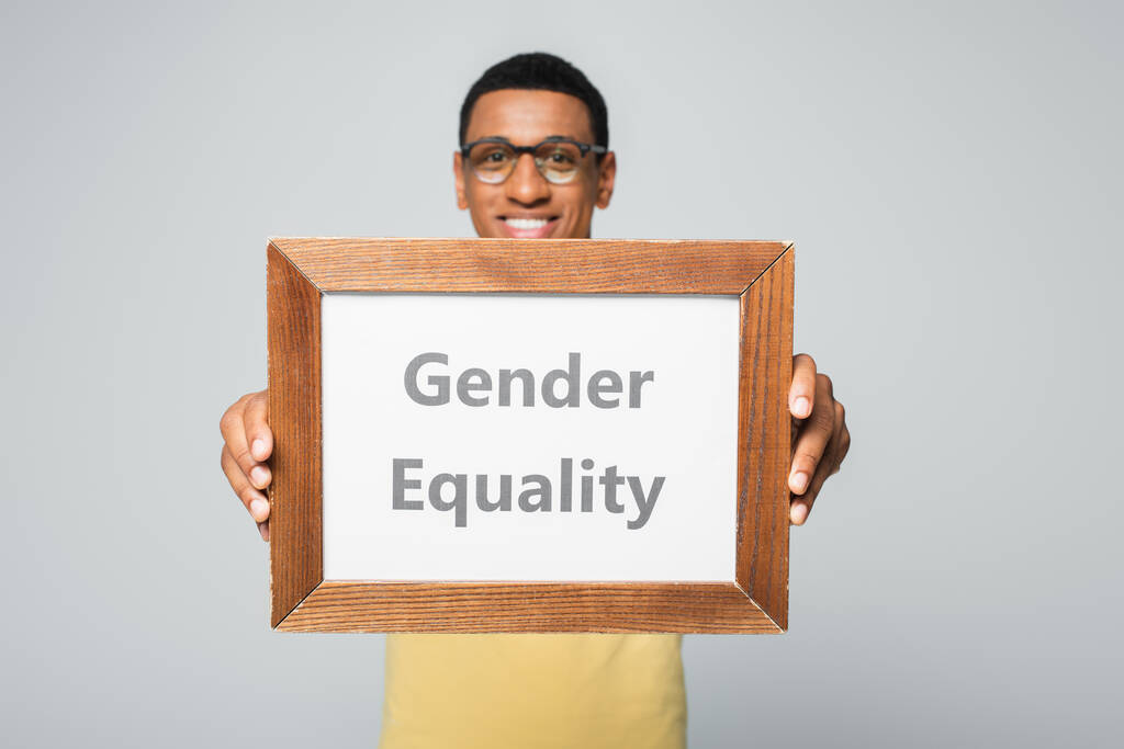 uomo afroamericano offuscata e felice tenendo cartello con la parità di genere lettering isolato su grigio - Foto, immagini