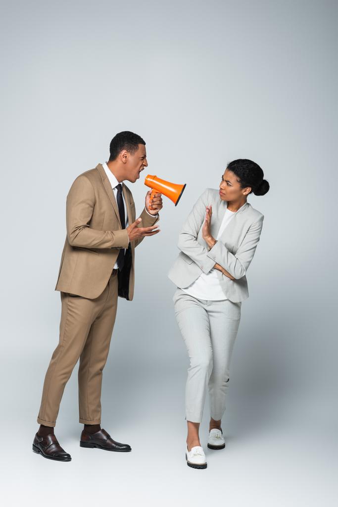 angry african american businessman screaming at businesswoman while holding megaphone on grey - Photo, Image