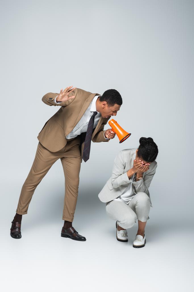 irritado Africano americano empresário gritando com assustado empresária enquanto segurando megafone em cinza - Foto, Imagem