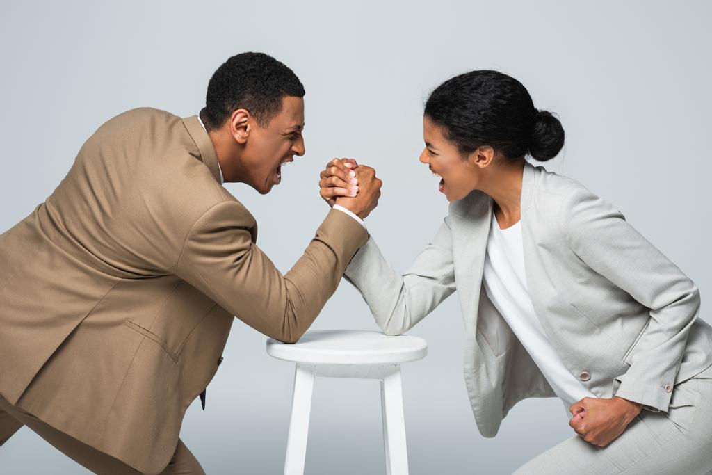 side view of african american businesswoman and man doing arm wrestling on white chair isolated on grey - Photo, Image
