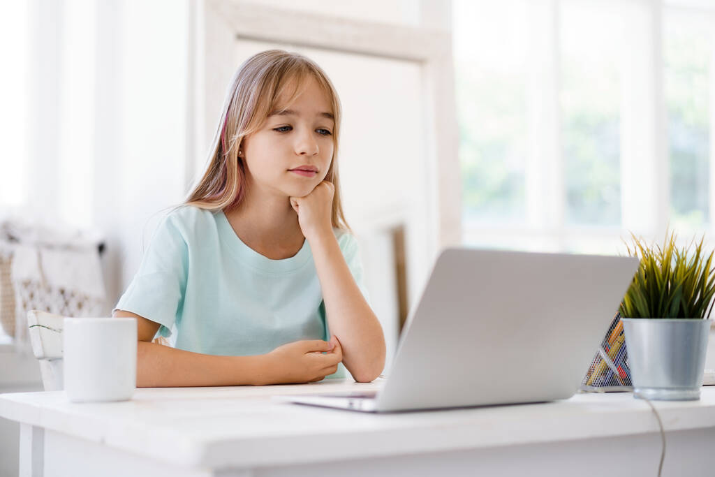 Ευτυχισμένο κοριτσάκι μαθητής χρησιμοποιώντας φορητό υπολογιστή στο σπίτι - Φωτογραφία, εικόνα