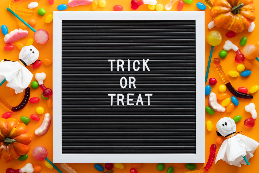 Trick or treat brievenbord met kleurrijke Halloween snoepjes en decoraties op oranje achtergrond. Platte lay, bovenaanzicht, overhead. Gelukkig Halloween concept. - Foto, afbeelding