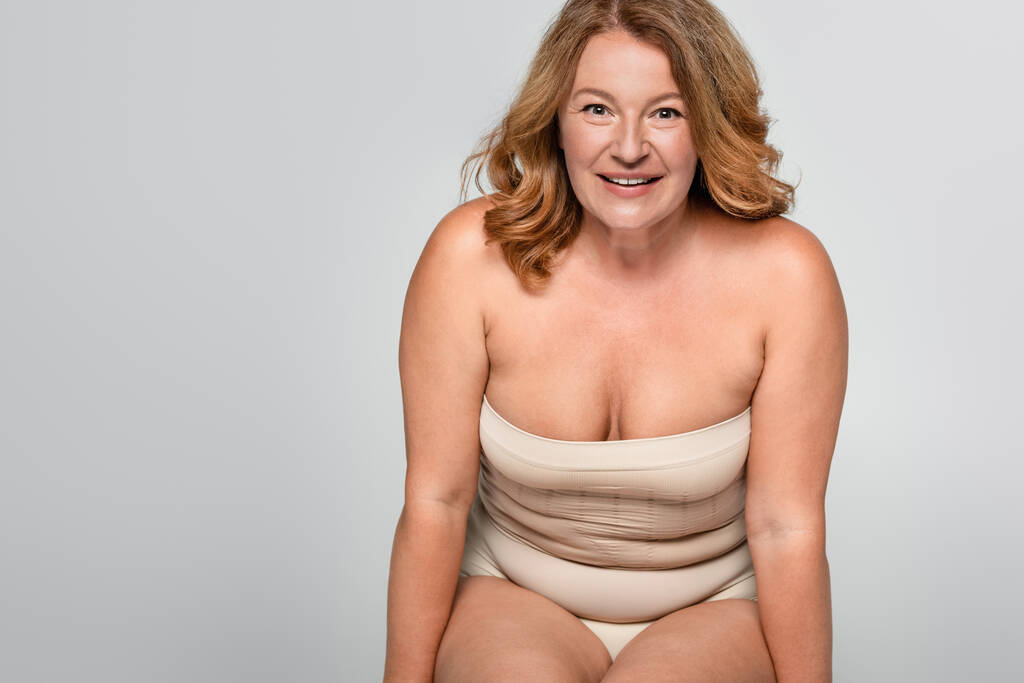 Lächelnde Frau mit Übergewicht, die isoliert auf grauem, körperpositivem Konzept in die Kamera blickt - Foto, Bild