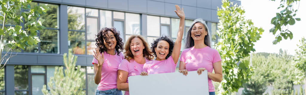Gelukkig multi-etnische vrouwen met roze linten houden plakband en zwaaien handen buiten, banner  - Foto, afbeelding