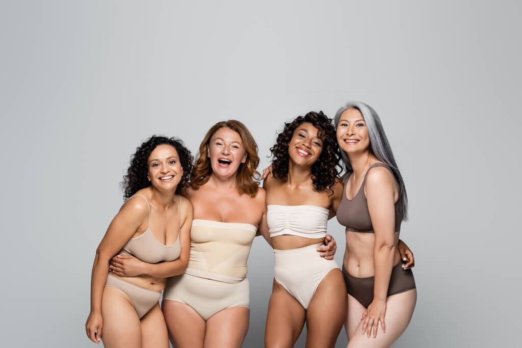 Multiethnic tělo pozitivní ženy v spodní prádlo objímání a pohled na kameru izolované na šedé  - Fotografie, Obrázek