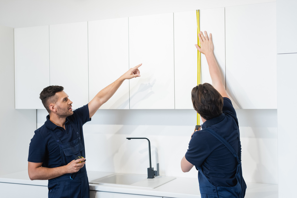ouvrier pointant vers collègue mesure meubles armoires dans la cuisine - Photo, image