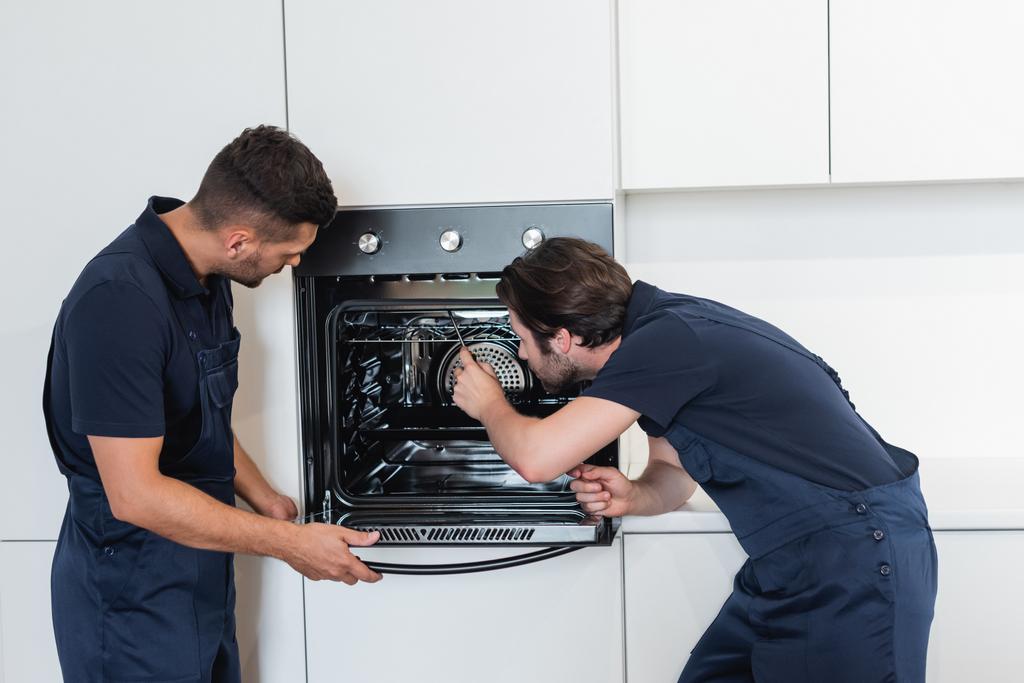 рабочие в комбинезоне ремонтируют электрическую духовку на кухне - Фото, изображение