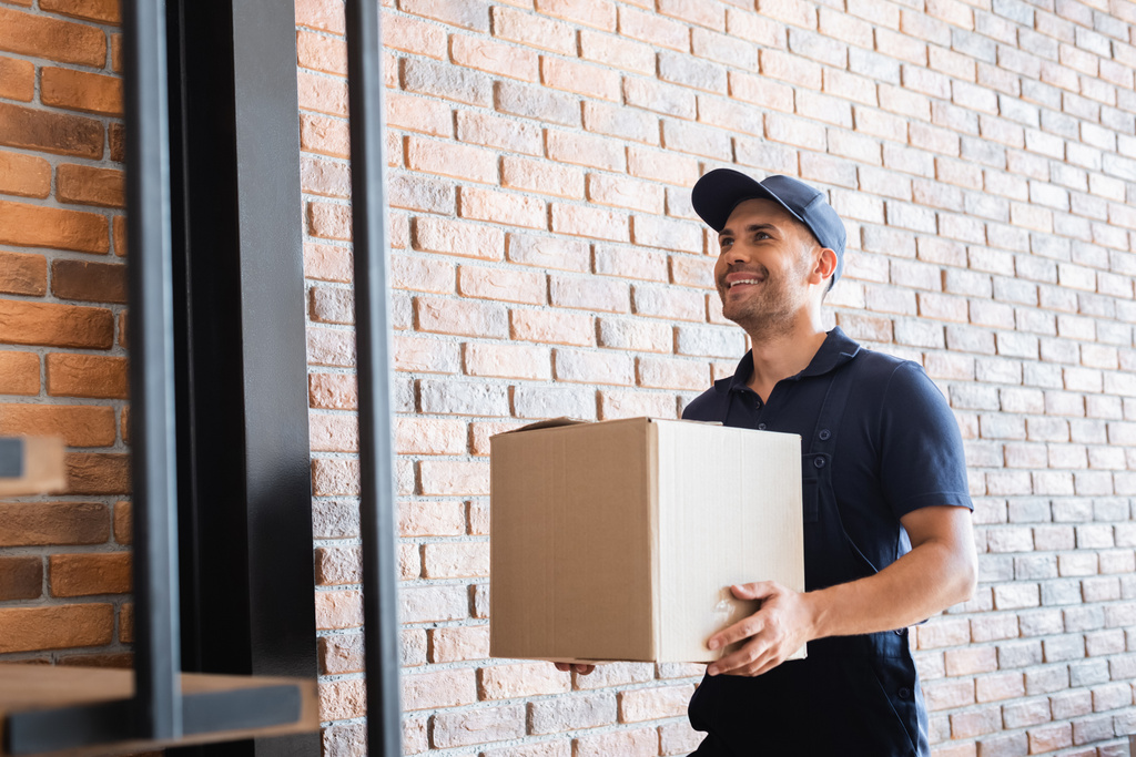 веселий чоловік доставки тримає картонний пакет біля цегляної стіни
 - Фото, зображення
