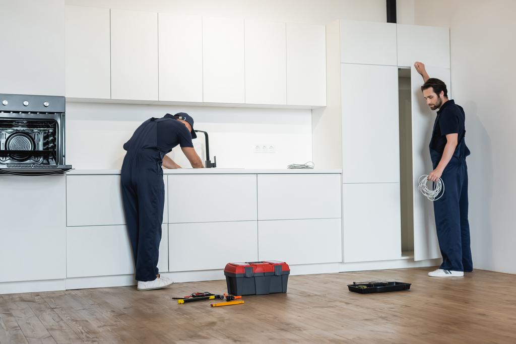putkimies ja sähköasentaja työskentelee modernissa keittiössä lähellä työkaluja lattialla - Valokuva, kuva