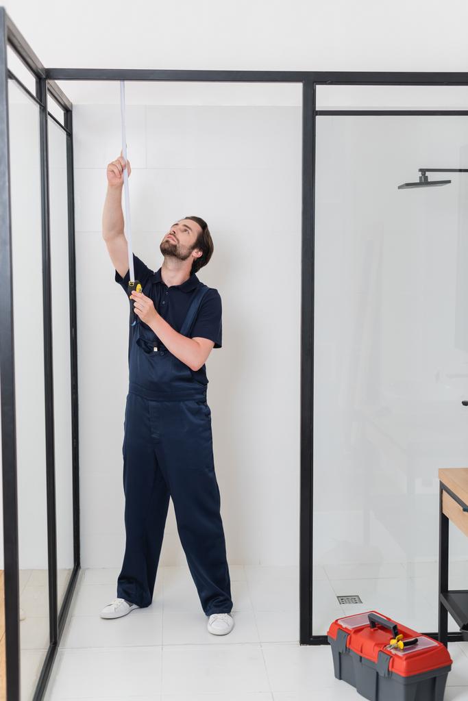 visão de comprimento total do trabalhador medindo cabine de chuveiro no banheiro - Foto, Imagem