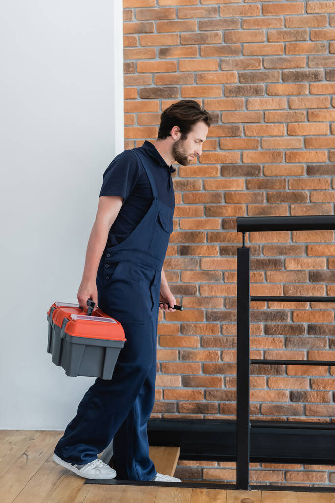 joven trabajador con caja de herramientas y linterna caminando abajo en apartamento  - Foto, Imagen