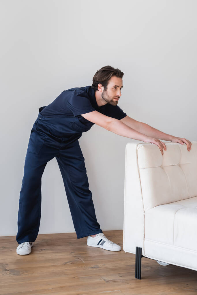 работник в форме движущийся белый диван в квартире  - Фото, изображение