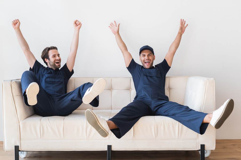 excited movers sitting on white couch with raised hands and legs - Photo, Image