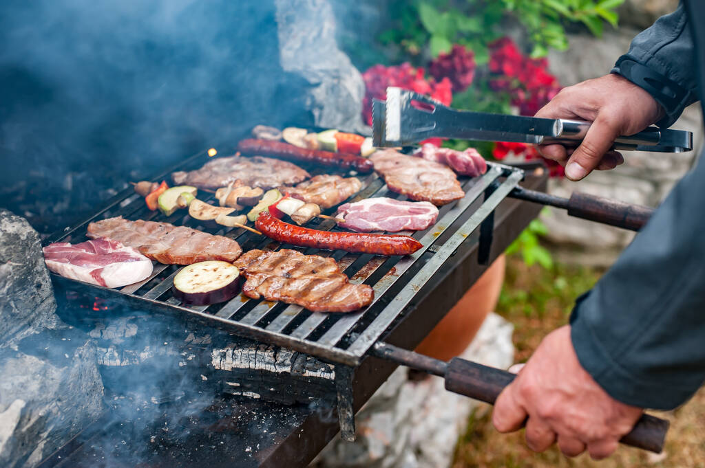 Hombre cocinar carne en la parrilla de barbacoa en la fiesta de barbacoa en el jardín de verano. Comida, personas y concepto de tiempo familiar - Foto, imagen
