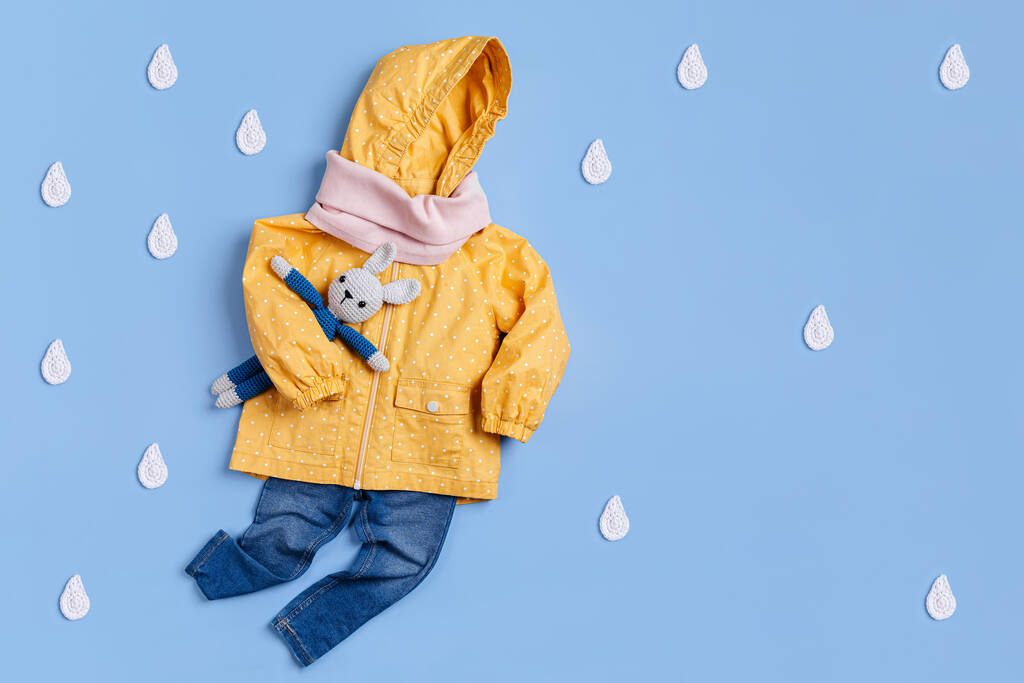 Leuke set van Herfst kinderen outfit. Gele regenjas met speelgoedkonijntje en jeans op blauwe achtergrond. Herfst stemming - Foto, afbeelding