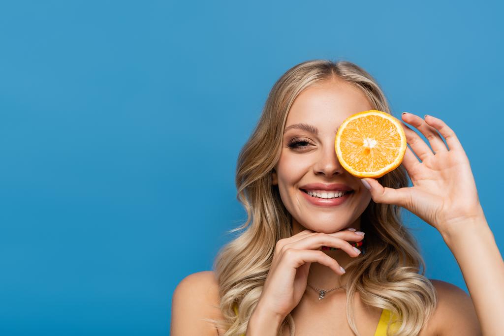 весела молода жінка, що прикриває око помаранчевою половиною, ізольована на синьому
 - Фото, зображення