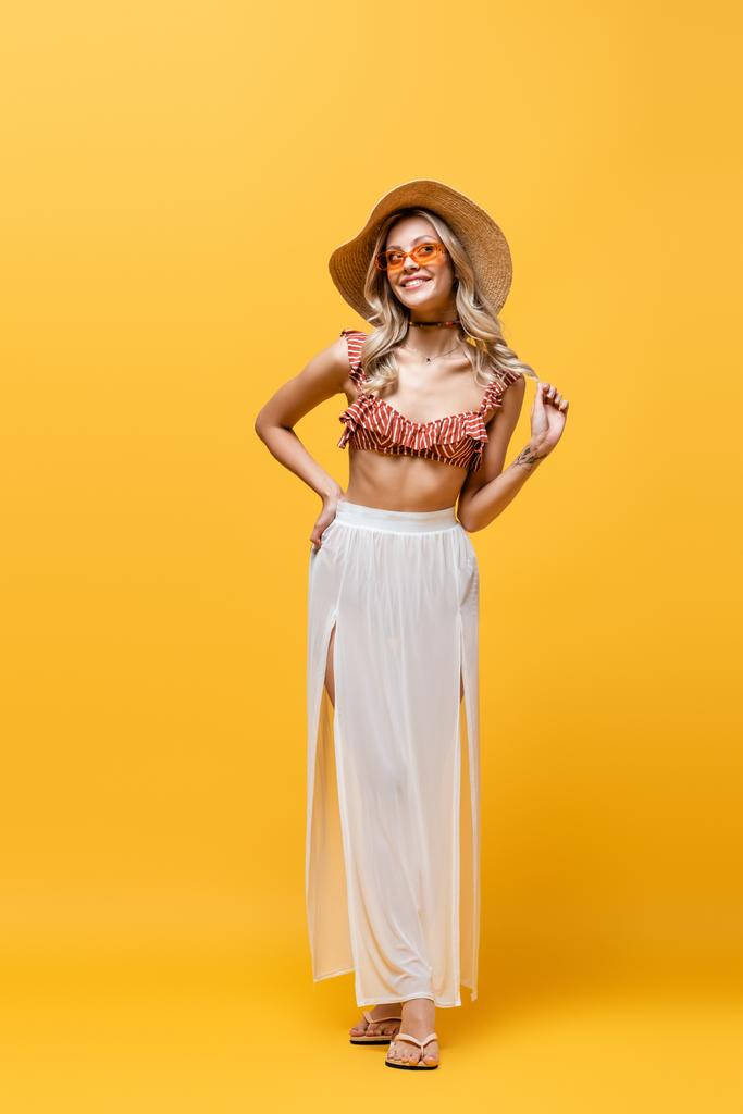 full length of smiling woman in ruffle bikini top and white skirt standing with hand on hip on yellow  - Photo, Image