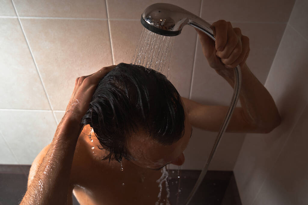 Genç yakışıklı adamın portresi kendini duş jeliyle yıkar, başını şampuanla yıkar. - Fotoğraf, Görsel