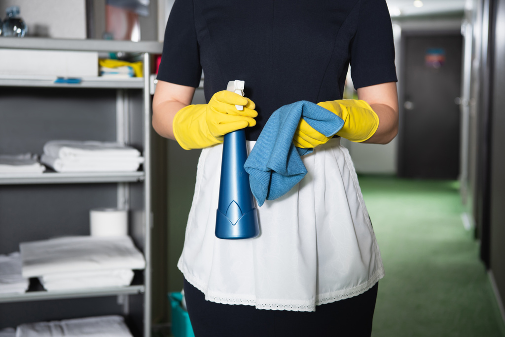 vista recortada de la camarera en guantes de goma sosteniendo botella de spray y trapo - Foto, Imagen