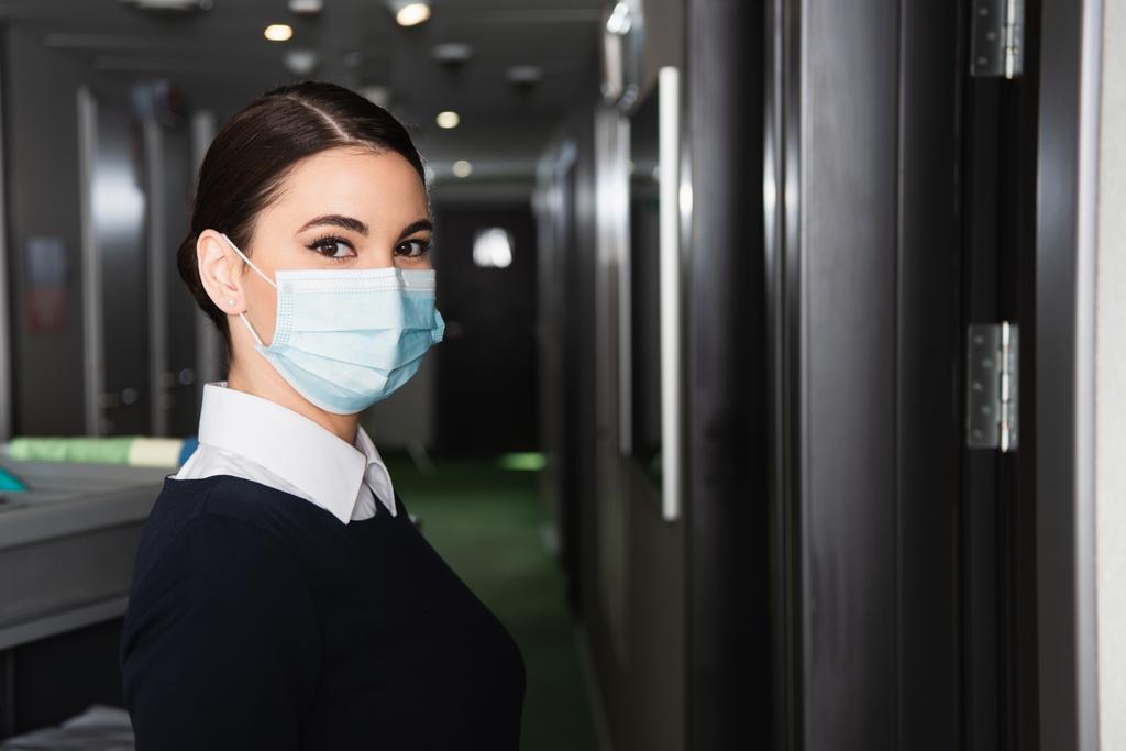 young maid in uniform and medical mask looking at camera - Photo, Image