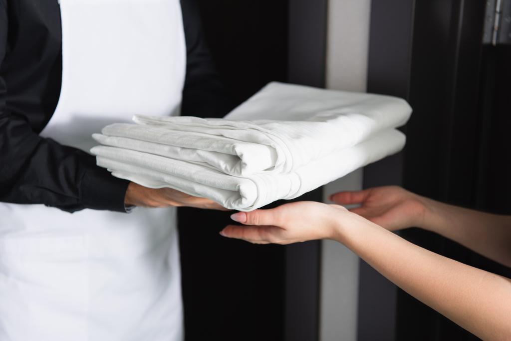 vista ritagliata di cameriera governante dando lenzuola pulite per la cameriera - Foto, immagini