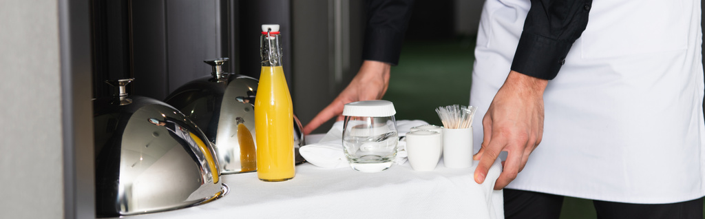 vista recortada del camarero en bandeja de entrega delantal con cloche y bebidas, pancarta - Foto, Imagen