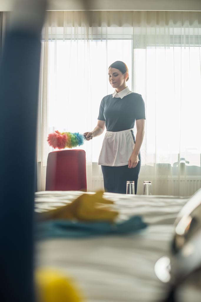 camareira em uniforme de limpeza poltrona vermelha com escova de poeira - Foto, Imagem