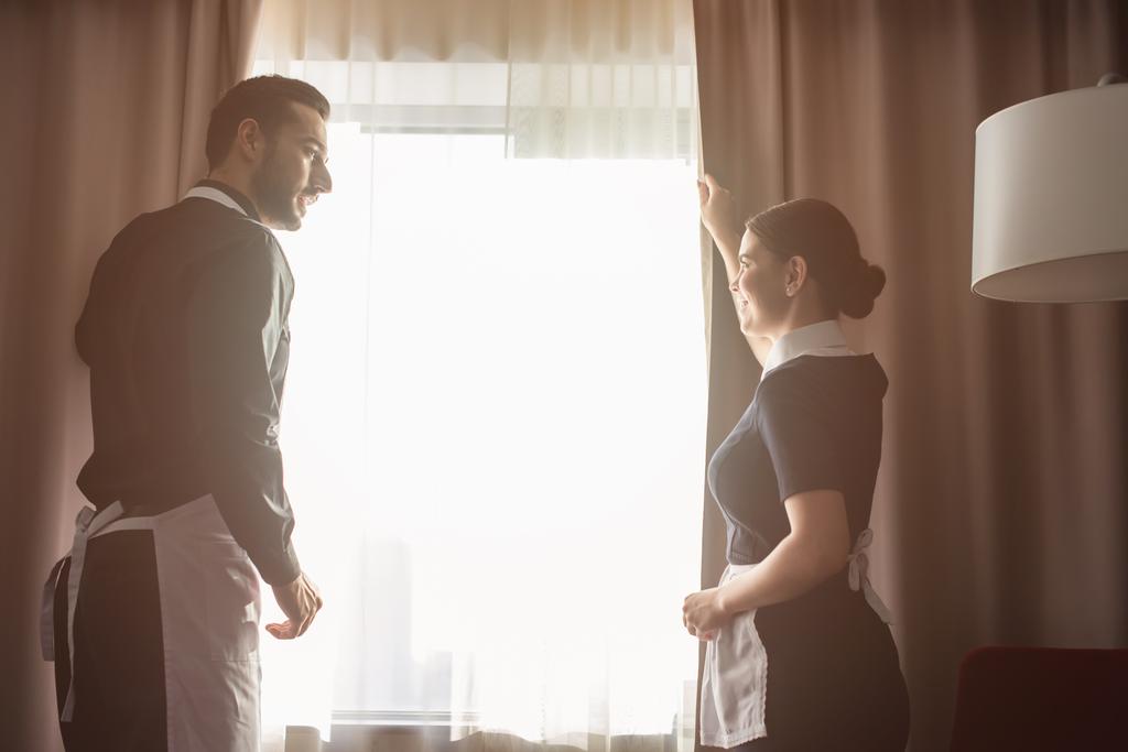 happy housekeepers adjusting curtains in hotel room  - Photo, Image