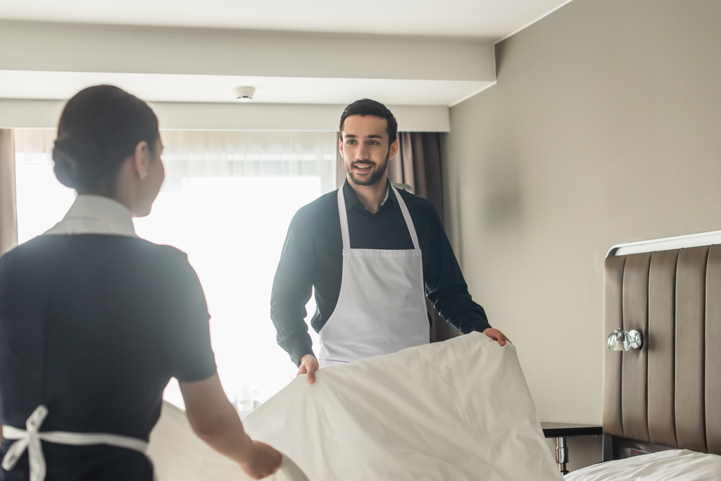 счастливые уборщицы меняют постельное белье в номере отеля  - Фото, изображение