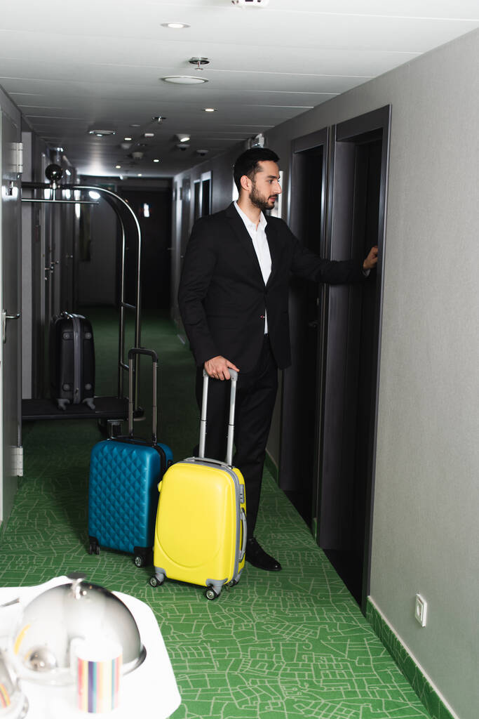 повна довжина дзвоника в костюмі, що стоїть біля багажу і стукає двері в готелі
 - Фото, зображення