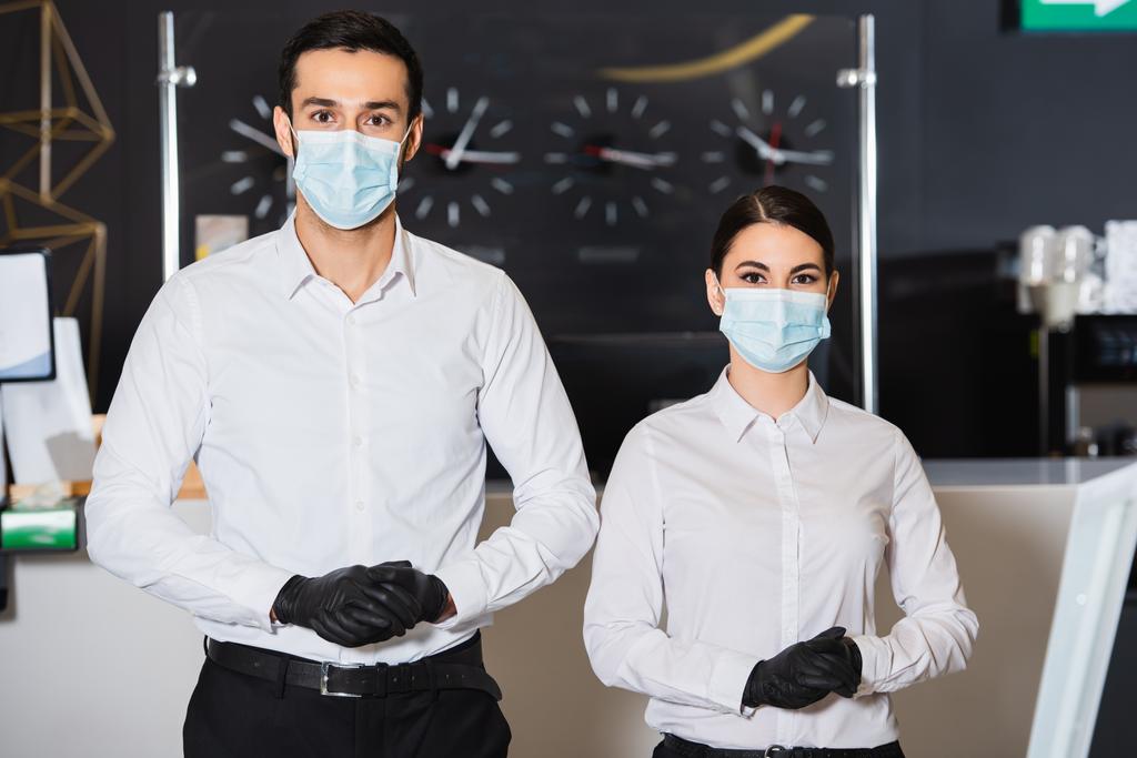 recepcjonistki w maskach medycznych i rękawiczkach lateksowych w pobliżu recepcji - Zdjęcie, obraz