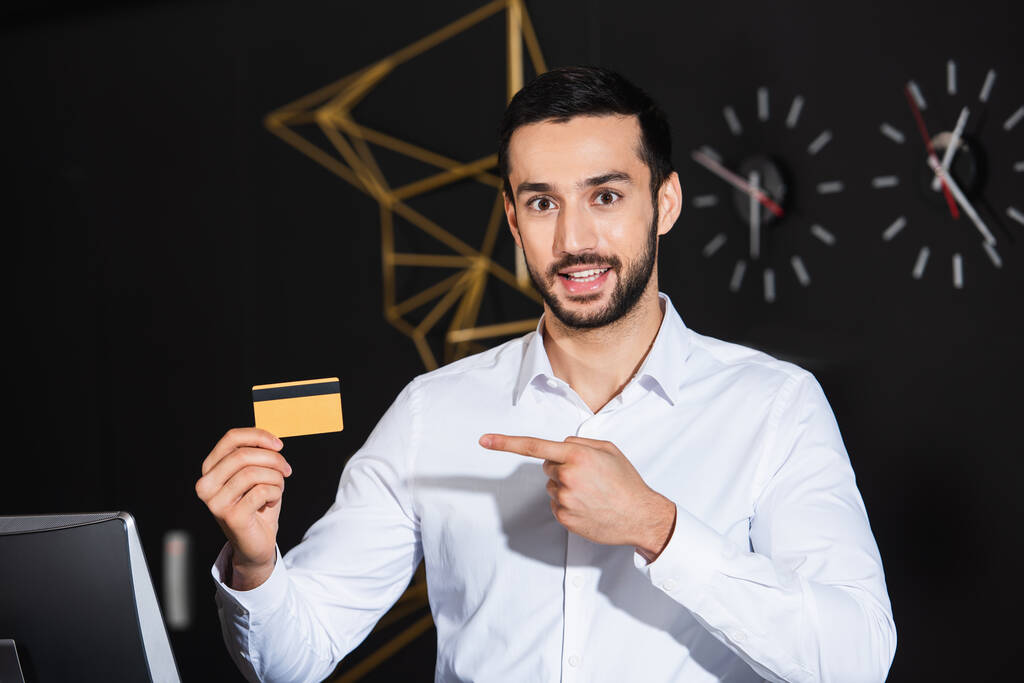 parrakas vastaanottovirkailija osoittaa luottokorttia ja hymyilee hotellissa  - Valokuva, kuva