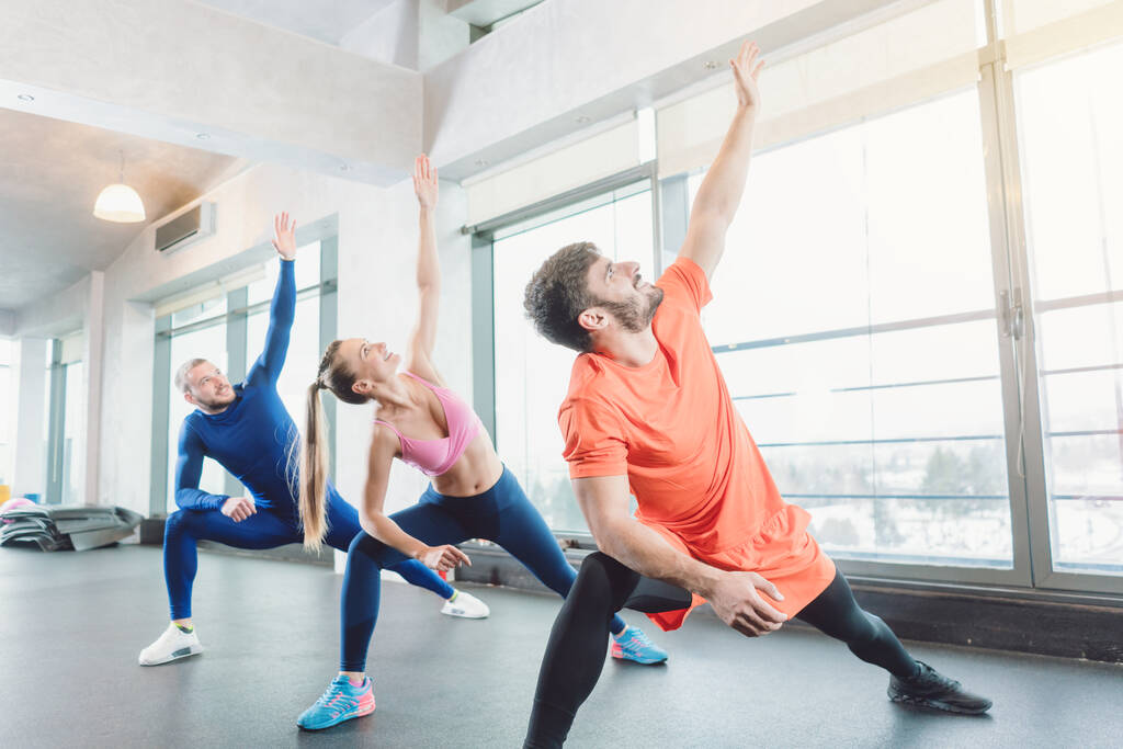 Fitnesslessen in een moderne en lichtgevende fitnessruimte met mensen die zich uitrekken - Foto, afbeelding