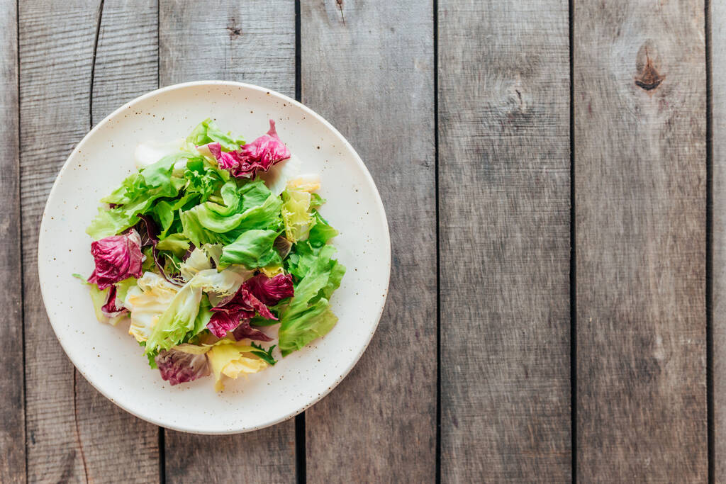 Healthy eating concept flat lay. Plate with mix of fresh green salad leaves, lettuce radicchio, basil on wooden background. Healthy eating concept. Vegetarian concept. Vegan food. Gardening concept. - Photo, Image