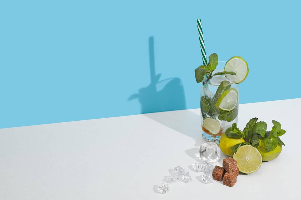 Mojito-Cocktail mit Limette, Minzblättern und Zuckerstücken auf doppeltem weiß-blauem Hintergrund mit Schatten. Kopierraum - Foto, Bild