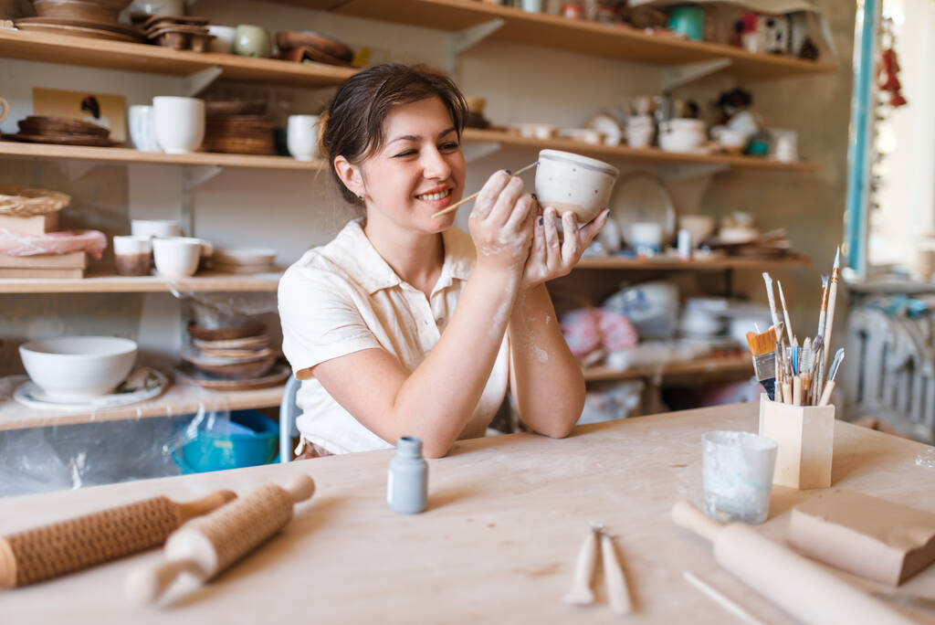 Vrouwelijke meester schildert een pot, aardewerk workshop. Een vrouw die een kom vormt. Handgemaakte keramische kunst, servies van klei - Foto, afbeelding