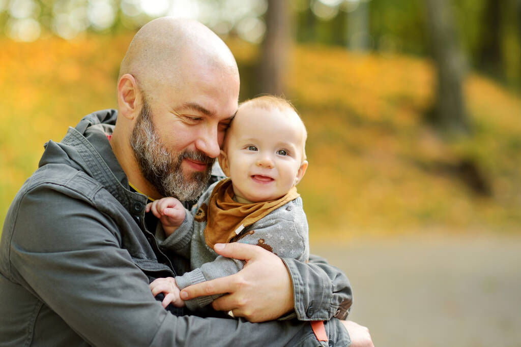 彼の父親の腕の中でかわいい赤ちゃんの男の子。市内の公園で晴れた秋の日にお父さんと息子が楽しんでいます。親愛なる息子が父親に抱かれて. - 写真・画像