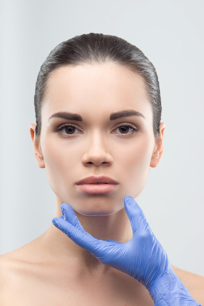 Kosmetikerin in Gummihandschuhen berührt Gesicht der jungen schönen wom - Foto, Bild