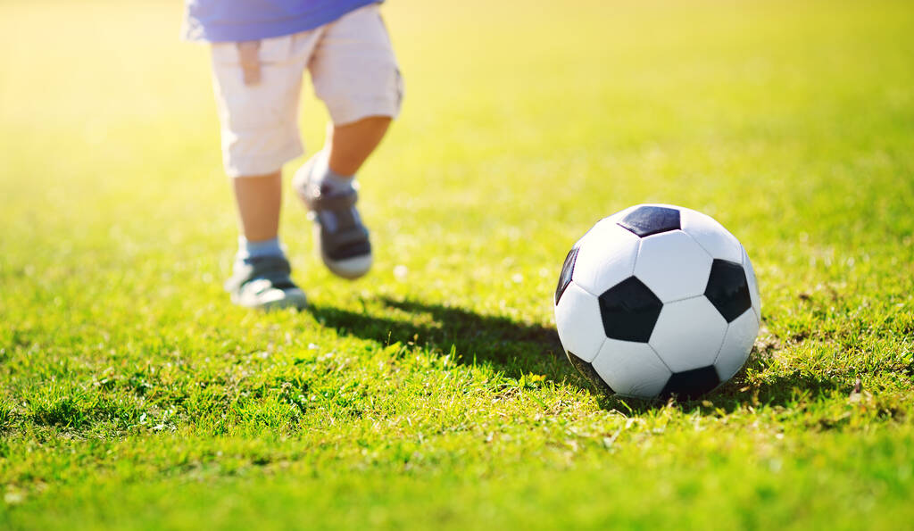 Un niño jugando al fútbol en el campo con puertas. Niño activo en verano con pelota - Foto, imagen