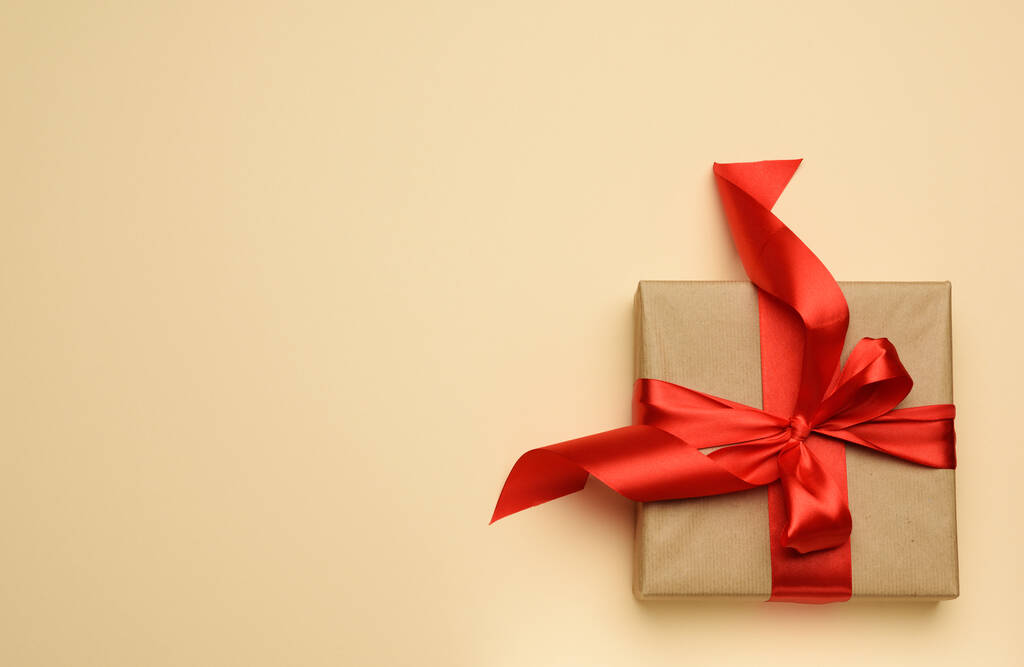 vierkante geschenkdoos is verpakt in rood papier en gekruld satijnen lint, feestelijke achtergrond, bovenaanzicht - Foto, afbeelding