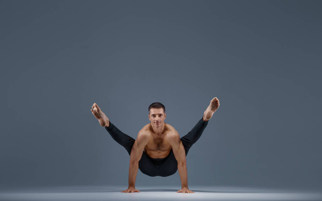 Yoga masculin faisant des exercices d'étirement en studio, fond gris. Homme fort pratiquant le yogi, l'entraînement asana, la concentration supérieure, un mode de vie sain - Photo, image