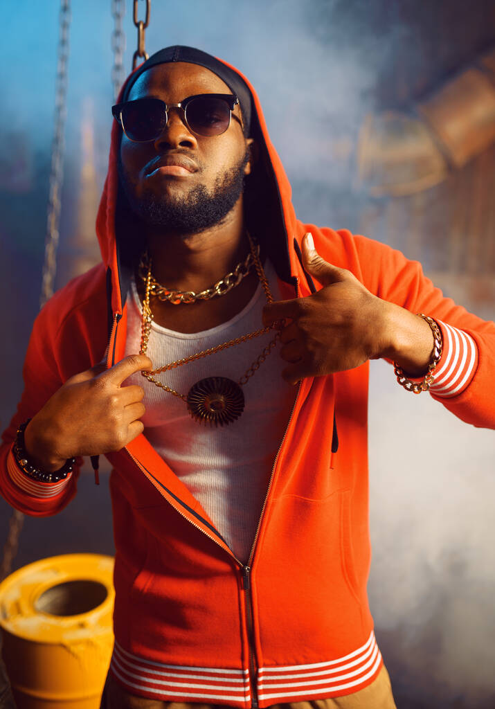 Rapper piros kapucnis pulcsiban és napszemüvegben a stúdióban, menő földalatti dekorációval. Hip-hop előadó, rap énekes, break-dance - Fotó, kép