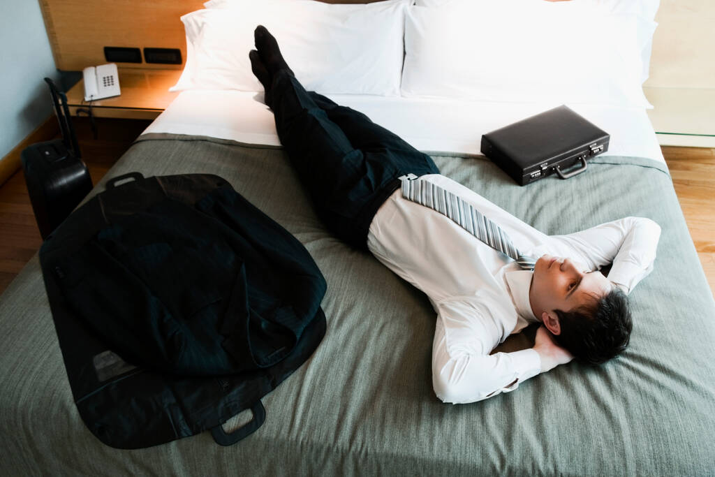 High angle view of a businessman resting on the bed with his hands behind his head - Photo, Image