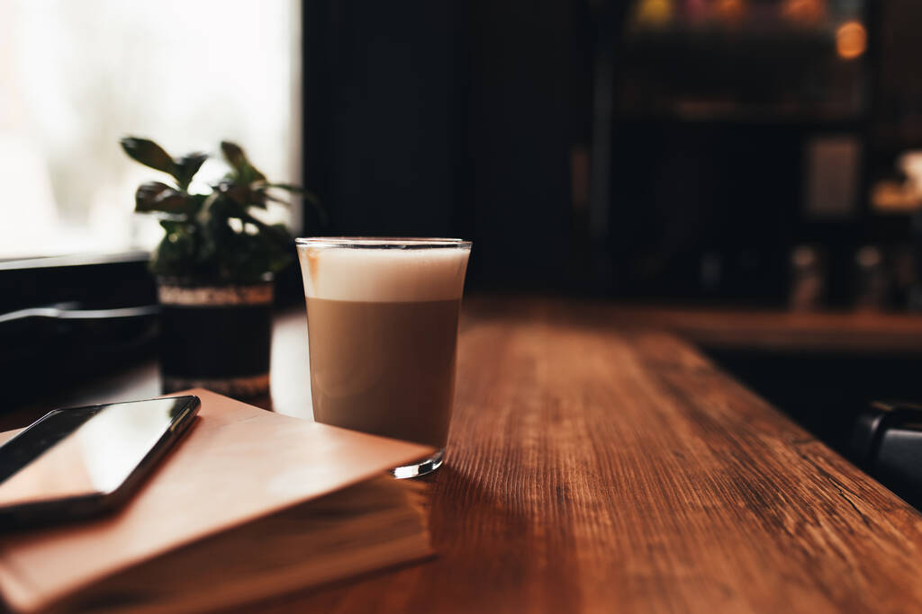 Tasse Kaffee, Notizbuch, Telefon am Tisch im Café. Unscharfer Hintergrund. Hochwertiges Foto - Foto, Bild