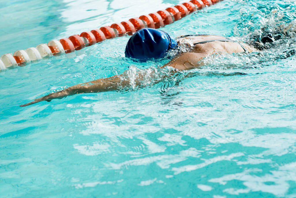 молода жінка в блакитній шапці і біле поло однорідне плавання у воді
 - Фото, зображення