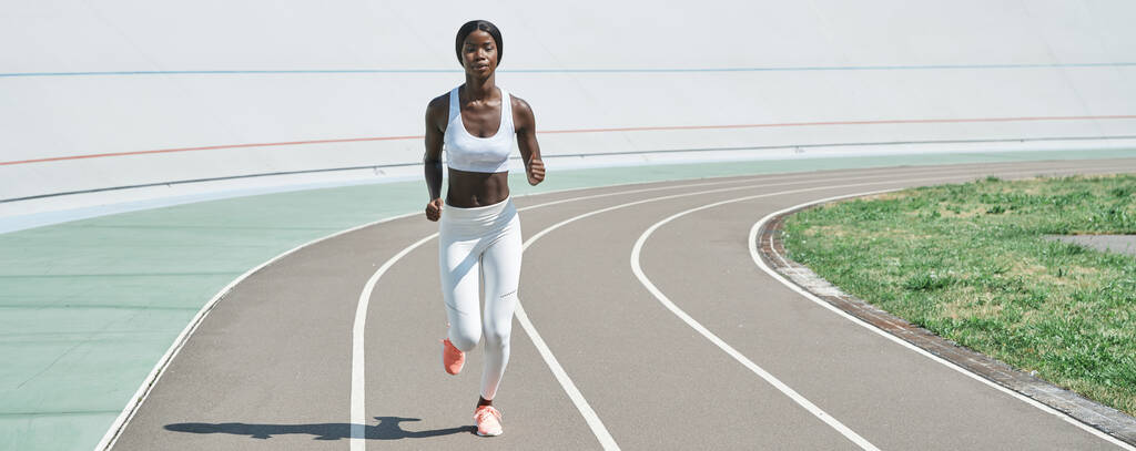 Comprimento total de bela jovem africana em roupas esportivas correndo na pista ao ar livre - Foto, Imagem