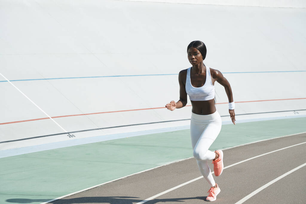 Luotettava nuori afrikkalainen nainen urheiluvaatteissa juoksee raiteillaan ulkona - Valokuva, kuva