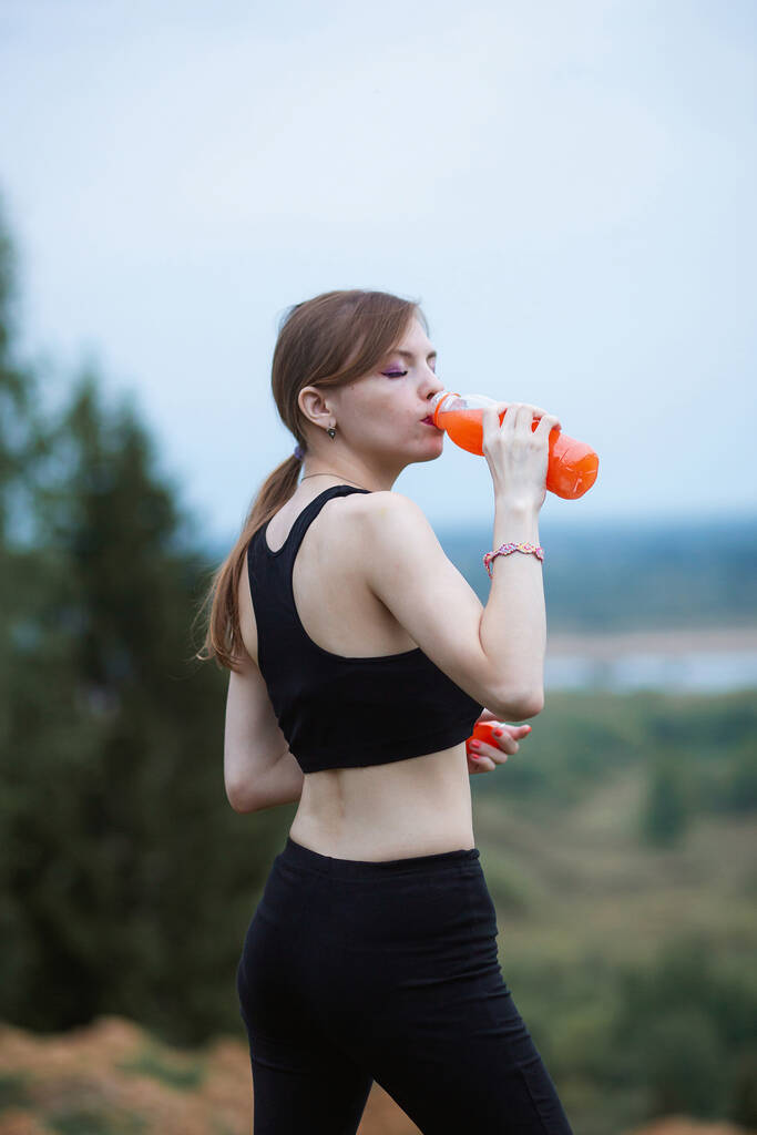 Femme portant des vêtements de sport s'hydrater en buvant du jus d'orange vibrant pendant l'entraînement. Soirée ou le matin dans la nature - Photo, image