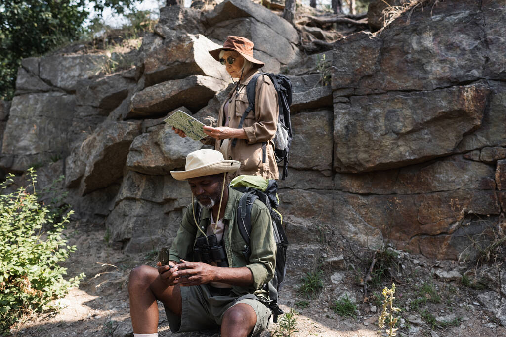 Старшие мультиэтнические туристы используют карту и компас возле скалы в лесу  - Фото, изображение